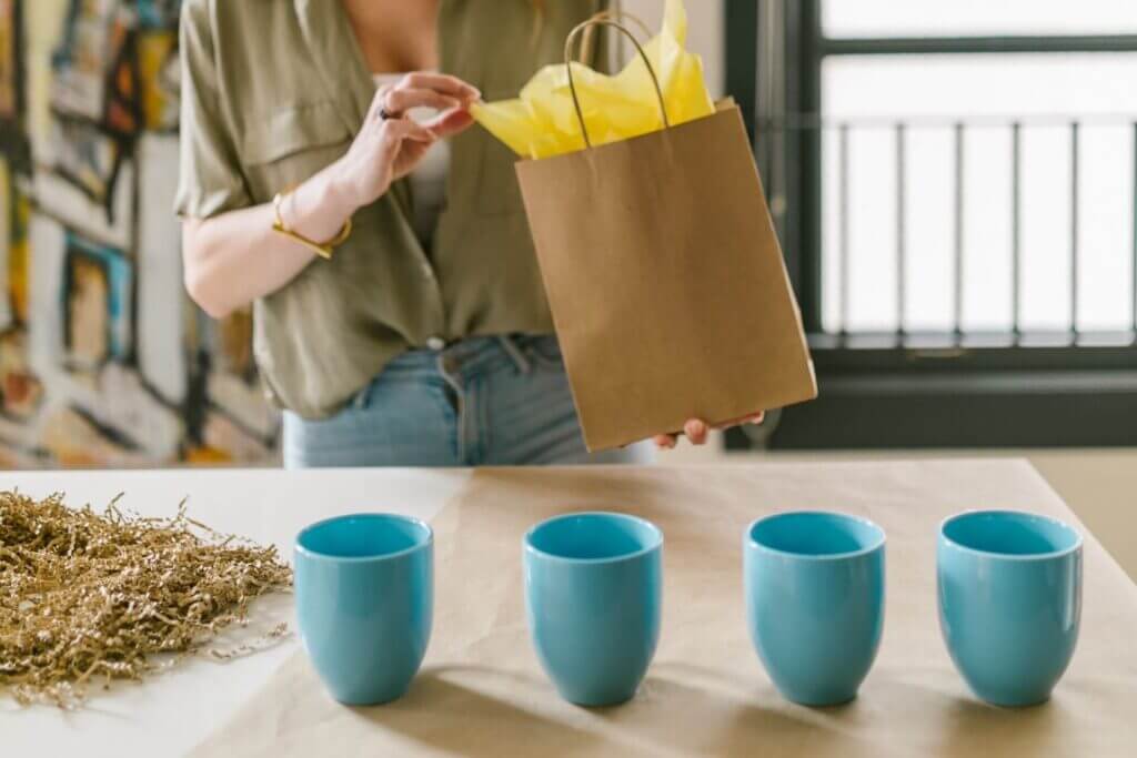 lady with paper bag and four blue mugs on table