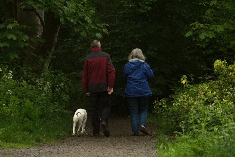 retired man and woman walking in countryside with dog not worrying about bills in retirement